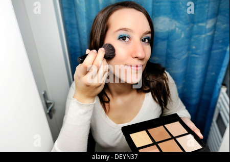 Young woman applying make-up in front of a mirror Stock Photo