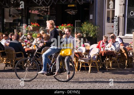 Customers sit outside Hotel de la Bourse restaurant cafe bar pub on Markt Maastricht Netherlands as a cyclist passes by Stock Photo