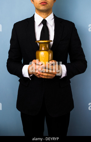 Young man in suit holding a wooden urn Stock Photo