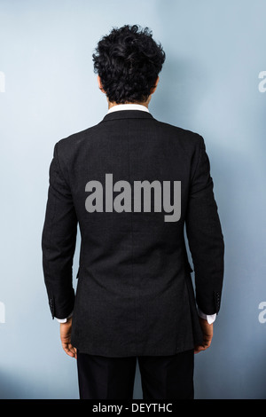 Rear view of young multi racial business man against a blue wall Stock Photo