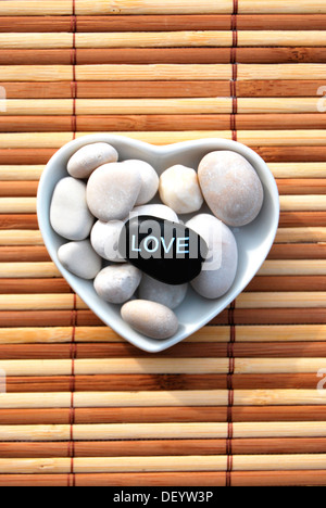 Hot stone massage stones, one labelled Love, in a heart-shaped porcelain bowl Stock Photo
