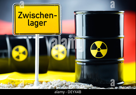 Three barrels of nuclear waste in front of a German flag and a town sign with the name 'Zwischenlager' Stock Photo