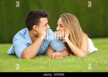 Couple in love dating and looking each other lying on the grass with a green background Stock Photo
