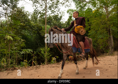 Buddhist monk on horseback with a begging bowl collecting alms in the morning, temple and monastery of Wat Phra Archa Thong or Stock Photo