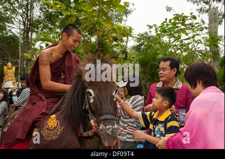 Buddhist monk on horseback collecting alms in the morning, temple and monastery of Wat Phra Archa Thong or Golden Horse Temple Stock Photo