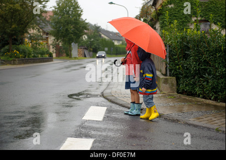 Two children, 3 and 7 years, crossing the street in the rain, Assamstadt, Baden-Wuerttemberg Stock Photo