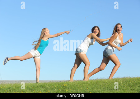 Group of teenager girls playing happy throwing water on the grass with the sky in the background Stock Photo