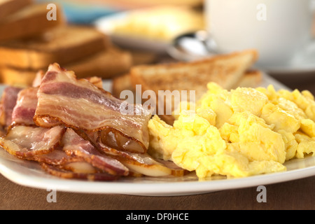 Fried bacon and scrambled eggs with toast bread in the back (Selective Focus, Focus on the lower edge of the bacon on top) Stock Photo