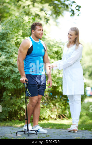 Pretty nurse looking at male patient trying to walk on his own in park Stock Photo