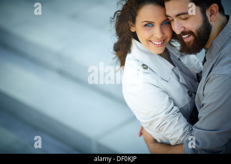 Image of happy woman looking at camera while being embraced by her sweetheart Stock Photo