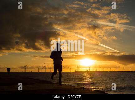 Man jogging at sunrise at North Gare near Seaton Carew. Teesside Offshore Windfarm at Redcar in distance. England, UK Stock Photo