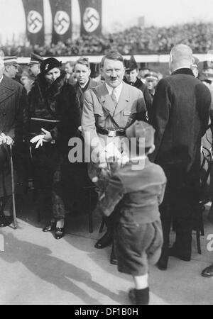 The image from the Nazi Propaganda! shows Adolf HItler being welcomed by a small boy on the occasion of the cornerstone laying ceremony for the Richard Wagner Memorial in Leipzig, Germany, 6 March 1934. To Hitler's left Winifred Wagner, the daughter-in-law of Richard Wagner. Fotoarchiv für Zeitgeschichte Stock Photo