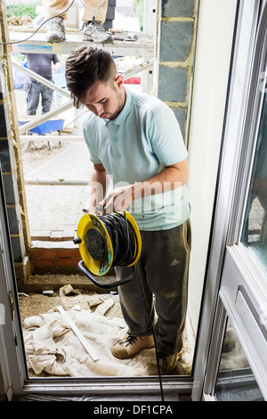 A worker using an extension cable drum in a newly constructed doorway of a house. Stock Photo