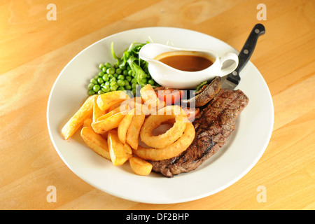 Traditional pub food - sirloin steak, onion rings and peas. Stock Photo