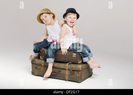 Two small cute brothers sitting on the suitcases Stock Photo