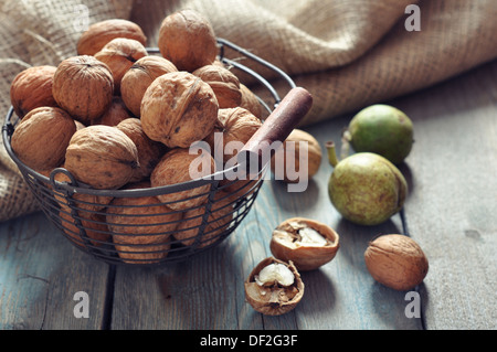 Whole and chopped walnuts in basket on old wooden background Stock Photo
