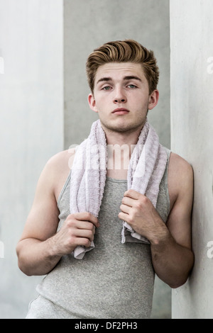 Young man with towel leans against concrete wall Stock Photo