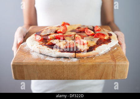 Woman's hands holds homemade pizza with tomato, bacon, salami and cheese. Wooden cutting board. Stock Photo