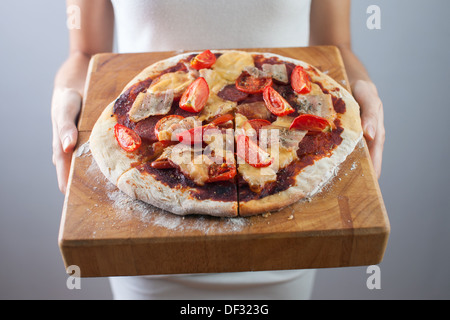 Woman's hands holds homemade pizza with tomato, bacon, salami and cheese. Wooden cutting board. Stock Photo