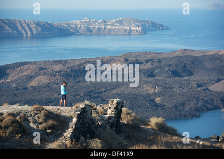 SANTORINI (THIRA), CYCLADES, GREECE. A holidaymaker photographing the view from the cliff-top village of Imerovighli near Fira. Stock Photo