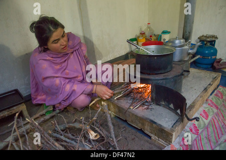 Young woman cooking on a fire inside of her house at Altit Village, near Karimabad, Hunza Valley, Gilgit-Baltistan, Pakistan Stock Photo