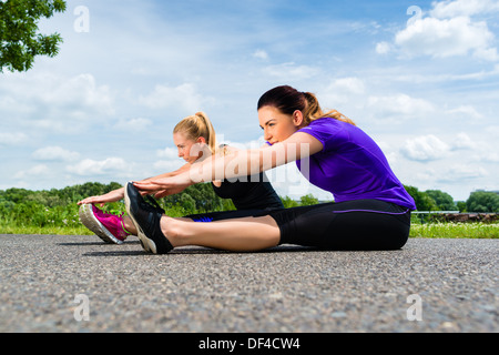 Urban sports - young women doing warming up together before running in the greenfield on a summer day Stock Photo