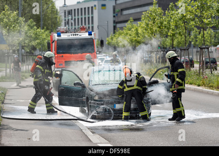 Firefighters are just putting out a burning and smoking car on the street Stock Photo