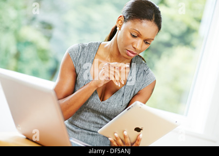Ethnic woman in office using iPad and laptop Stock Photo
