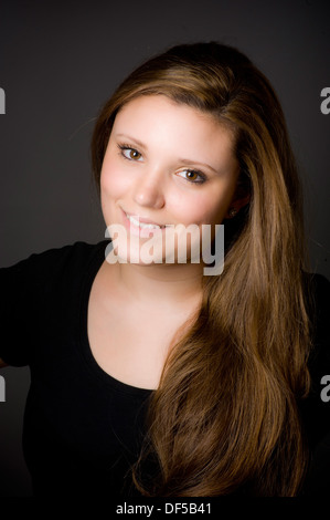 Young caucasian woman with long, light brown hair swept over her shoulder looking at camera smiling. Stock Photo