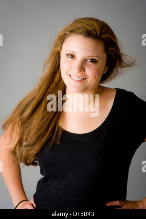 Young caucasian woman with long, light brown hair swept over her shoulder looking at camera smiling. Stock Photo