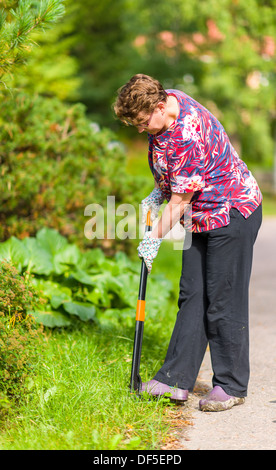 Woman in the garden pulling weeds out with the gardening equipment Stock Photo