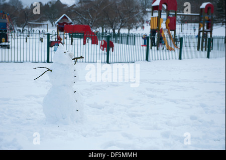 Cold winter scene with solitary snowman standing by children's play area in fresh white snow - Ilkley park, West Yorkshire, England, UK. Stock Photo