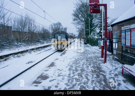 Train arriving & pulling into deserted railway station after snowfall,  footprints on platform & snow on tracks - Baildon, Shipley, England, UK. Stock Photo