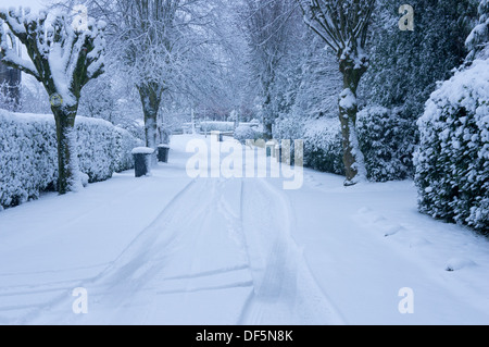 Winter wonderland scene - quiet tree-lined, residential street with road & pavements, covered in blanket of white, fresh snow - Guiseley, England, UK. Stock Photo