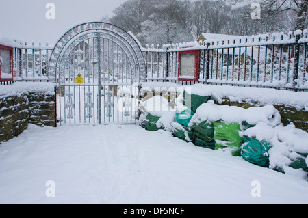 Garden refuse sacks piled by decorative snow-covered wrought iron gates on snowy winter day - entrance to Hall Cliffe Community Gardens, Baildon, UK. Stock Photo