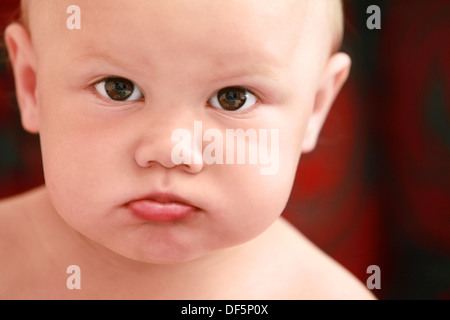 Serious Caucasian baby girl close-up portrait on dark blurred background Stock Photo