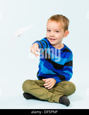 Happy boy playing with paper airplane in studio, light blue background Stock Photo
