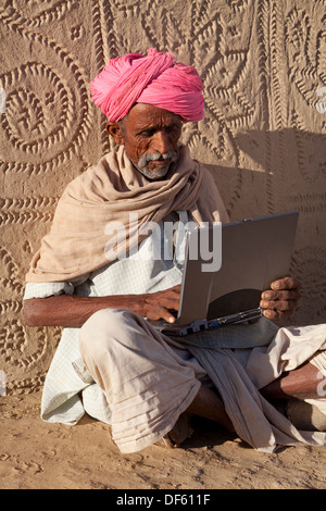 india, Rajasthan, Thar Desert, Village elder using laptop in front of decorated wall Stock Photo