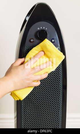 Vertical photo of female hand cleaning home air purifier with yellow microfiber rag with wall in background Stock Photo