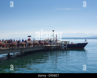 Nyon, a Swiss town on the shores of Lake Geneva, flower decorated pier with people lining up for a trip on the lake Stock Photo