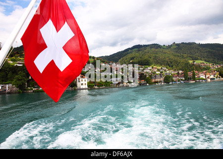 A Swiss flag flies from the stern of a lake steamer as it leaves the town of Oberhofen on Lake Thun. Stock Photo