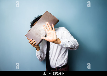 Young man doesn't want his photo taken and is hiding his face behind a briefcase Stock Photo