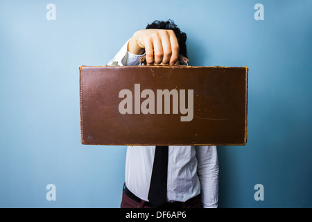 Young businessman holding an old briefcase in front of his face Stock Photo