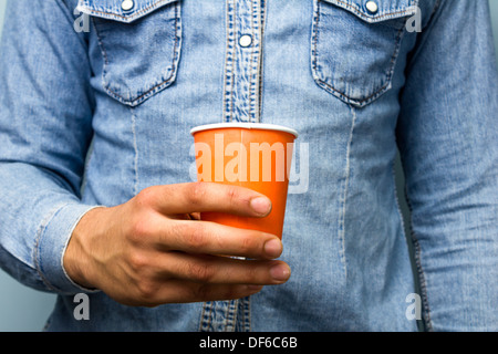Close up on man in blue denim shirt holding an orange paper cup Stock Photo