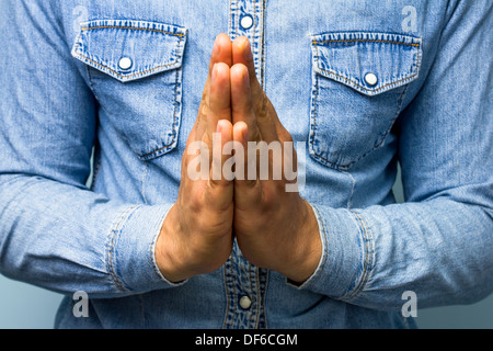 Young man in blue denim shirt with his hands clasped in prayer Stock Photo