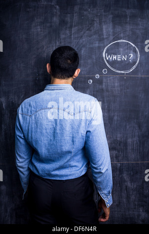 Rear view of young man standing by blackboard with the word when written on it Stock Photo