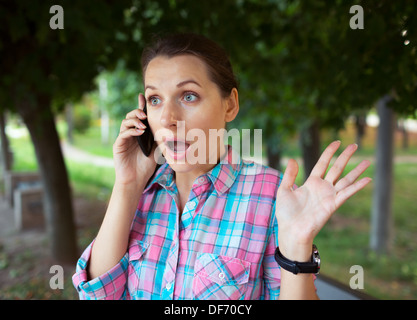 Portrait of surprised beautiful woman in the park talking on the phone Stock Photo