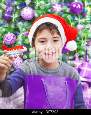 Portrait of cute arabic boy enjoying Christmastime gift, playing with little plastic airplane, wearing red Santa hat Stock Photo