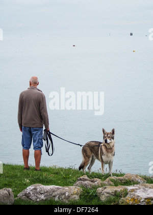A man stands with a Husky on a lead looking out to sea from a hilltop in Southsea Hampshire, England Stock Photo