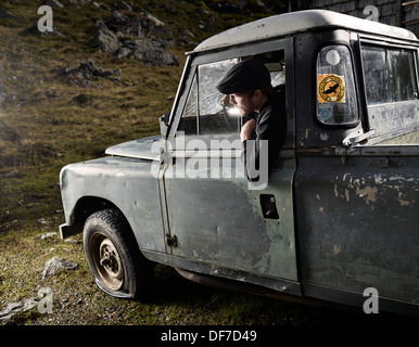 Man with a hat sitting in the driver's seat of an old car noticing a flat front left tyre, Inneralpbach, Tyrol, Austria Stock Photo